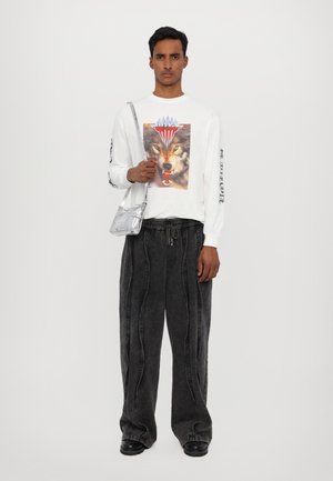 Long-sleeve white shirt with graphic of a wolf, black wide-leg pants with seams, and a silver crossbody bag. Black shoes complete the outfit.