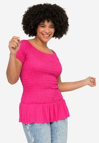 Fuchsia peplum-top med en samlet tekstur og korte ærmer, lavet af blødt stof, parret med lyst vaske jeans med blomsterbroderi.