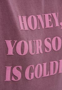 Purple fabric featuring large, raised pink text that reads, "HONEY, YOUR SOUL IS GOLDEN," with a smooth texture and subtle sheen.