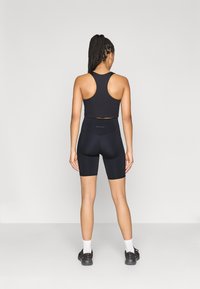 Musta urheilullinen croptop ja korkeavyötäröiset pyöräilyshortsit, molemmat joustavasta materiaalista. Lyhyet hihat, racerback-malli ilman näkyviä kuvioita.