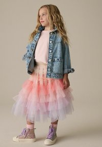 Giacca di denim, t-shirt rosa, gonna in tulle a strati in rosa pastello e bianco, e sneakers alte scintillanti con lacci lavanda.