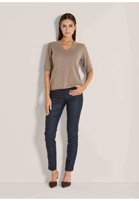 Beige V-hals gebreide top met korte mouwen gecombineerd met marineblauwe slim-fit broek en loafers met luipaardprint, tegen een neutrale achtergrond.