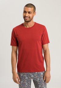 T-shirt rossa a maniche corte in tessuto morbido con colletto rotondo, abbinata a pantaloni grigi a fantasia caratterizzati da design floreali in blu e bianco.