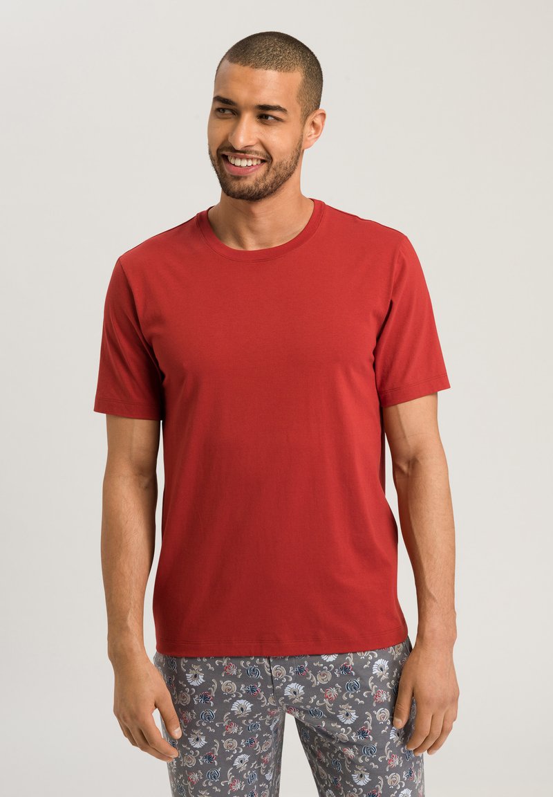 Rød kortærmet t-shirt i blødt stof med rund hals, parret med mønstrede grå bukser med blomsterdesign i blå og hvid.