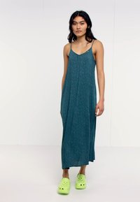 Robe maxi à imprimé floral teal avec des bretelles fines, un design fluide et une coupe ample ; assortie à des sabots verts vif. Tissu léger et lisse.