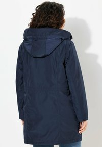 Giacca impermeabile blu navy con cappuccio, caratterizzata da una texture liscia e lucida, vita elasticizzata e due tasche laterali.