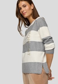 Gestreifter Pullover in Grau und Weiß mit leicht lockerem Schnitt. Verfügt über gerippte Bündchen und Saum, glänzende Schriftzüge und seitliche Schlitze für mehr Komfort.