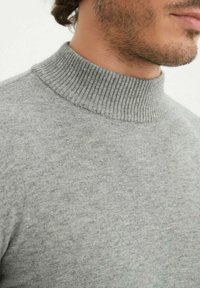 Pull en col roulé gris en tissu doux et texturé. Présente un col côtelé, un corps lisse et un motif subtilement chiné.