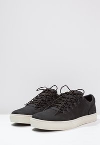 Baskets en cuir noir avec bout rond, lacets plats et semelle en caoutchouc. Dotées d'œillets métalliques et d'accents de couture le long de la semelle intermédiaire.