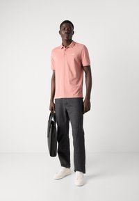 Chemise polo rose à manches courtes avec un col, assortie à un jean gris foncé et des baskets blanches ; portant un sac noir.