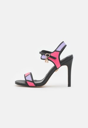 Sandalia de tacón alto negra con detalles coloridos en rosa y morado, diseño geométrico, correa ajustable en el tobillo y una hebilla decorativa.