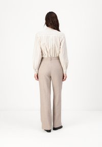 Pantalons beiges taille haute avec une coupe droite, associés à une chemise blanche à rayures et à boutons. Texture lisse et coupe ajustée.