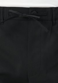 Black pants featuring a smooth texture, a button closure, and a fabric tie at the waist with a side pocket visible.