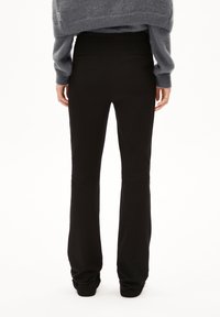 Schwarze, ausgestellte Hosen mit glatter Textur, mittelhoher Taille und zwei Gesäßtaschen, kombiniert mit einem grauen, kurz geschnittenen Pullover.