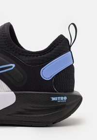 Zwarte sportieve schoen met een gestructureerde bovenkant, blauwe accenten en een opvallende zwarte zool met het label "NITRO INFUSED."