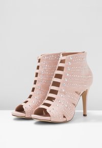 Botines abiertos de ante rosa con diseño de cortes, adornados con varios tamaños de brillantes rhinestones, que cuentan con un tacón de aguja.