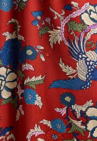 Roter Stoff mit aufwendigen Blumenmustern in Blau, Weiß, Rosa und Grün, verziert mit stilisierten Vögeln und Blättern über die gesamte Fläche.