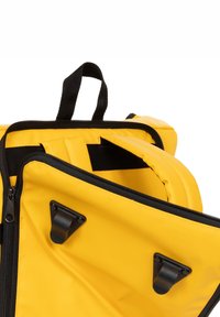 Mochila amarilla con cremalleras y herrajes negros. El exterior es de nylon liso con un compartimento principal y un bolsillo adicional. Correas ajustables.