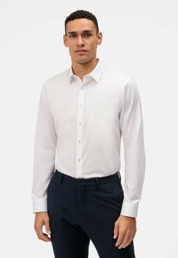 Witte lange mouwen shirt met een klassieke kraag, knoopsluiting aan de voorkant en subtiele glans. Gecombineerd met marineblauwe broeken, met een platte voorkant en riemlussen.