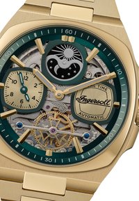 Goudkleurig automatisch horloge met een groene wijzerplaat en twee sub-dials, intrigerende tandwieldetails, zon- en maanmotieven, en een gestructureerde metalen bracelet.