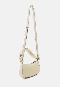 Piccola borsa a tracolla in pelle bianco sporco con base curva, tracolla lunga regolabile e zip e borchie in metallo dorato.