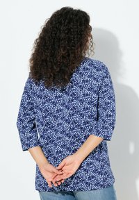Niebieski top w kwiatowy wzór z rękawami 3/4, wykonany z lekkiego materiału. Charakteryzuje się luźnym krojem i zaokrąglonym dołem, odpowiedni na co dzień.