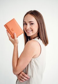 Orange leather wallet with embossed logo, held in one hand. Simplistic design with smooth texture, set against a light background.