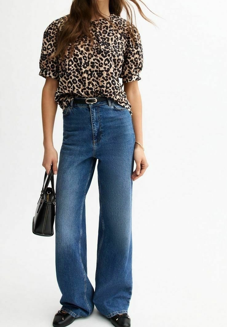 Camicetta con stampa leopardata, vestibilità ampia, maniche corte; jeans blu a vita alta e gamba larga; borsa nera; scarpe nere a punta.