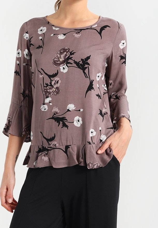 Blus med blommönster i mauve med trekvarts trumpetärmar. Har en volangsnitt i nederkant och en rundad halslinning. Tillverkad av lättviktsmaterial.