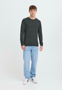 Suéter gris oscuro de manga larga con cuello redondo, puños y dobladillo acanalados, combinado con jeans azul claro y zapatillas blancas con rayas negras.