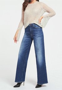 Light beige, loose-knit sweater with wide sleeves. Paired with high-waisted, wide-leg denim jeans in medium blue. Black pointed heels.