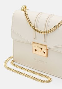 Borsa in pelle beige con una tracolla in catena dorata, caratterizzata da una chiusura dorata e cuciture decorative sul davanti, logo impresso sul fondo.