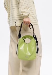 Lśniąca zielona torebka z zaokrąglonym dnem, wyciętym uchwytem i odpinanym czarnym paskiem. Zawiera nazwę marki "BIMBA Y LOLA" w kolorze srebrnym.