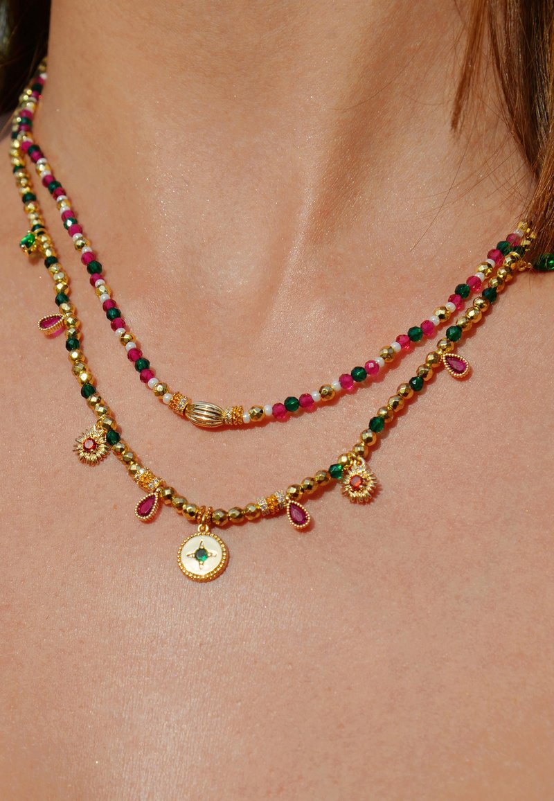 Collier en métal doré à plusieurs couches, orné de perles colorées vertes, roses et blanches, avec des charms décoratifs et un pendentif central.