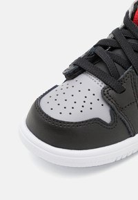 Sneaker in pelle nera con accenti grigi, punta perforata e suola intermedia bianca. Presenta lacci neri e una fodera in tessuto rossa.