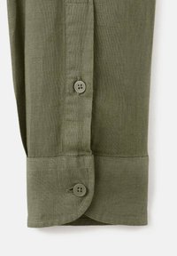 Manga de camisa de lino verde oliva con dos botones, con un diseño estructurado y una tela texturizada. Detalle de costura a lo largo de los bordes.
