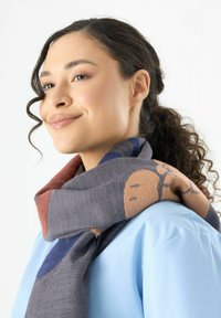 Gestrickter Schal in Grau, mit einem grafischen Design und tanfarbenen sowie blauen Akzenten. Weicher Stoff, ordentlich um den Hals gewickelt.