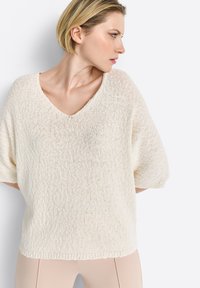 Cremfarbener, lockerer Strickpullover mit V-Ausschnitt, kurzen Ärmeln und einer strukturierten Oberfläche. Akzente setzen einen dezenten gerippten Saum.