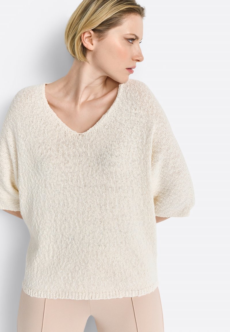 Cremfarbener, lockerer Strickpullover mit V-Ausschnitt, kurzen Ärmeln und einer strukturierten Oberfläche. Akzente setzen einen dezenten gerippten Saum.