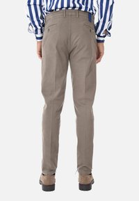 Pantaloni in cotone beige con vestibilità a gamba dritta, dotati di tasche posteriori e una leggera lucentezza, abbinati a scarpe color cammello.