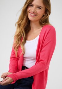 Roze cardigan met lange mouwen en open voorkant. Draag het over een witte top, met een zachte textuur en een comfortabele pasvorm.