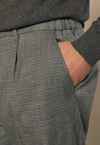 Grau karierte Hose mit lässiger Passform, ausgestattet mit Seitentaschen und einer glatten Textur. Der Bund hat dezente Falten für zusätzliche Details.
