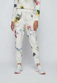 Blommönstrade sweatpants i vitt tyg, med flerfärgad botanisk tryck och elastiska muddar, i kombination med ljusa sneakers.