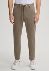 Beige chinos met een elastische tailleband, toelopend bij de enkels, gecombineerd met witte sneakers. Glad materiaal met een subtiele textuur.