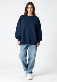 Navy zilas oversize krekls ar apaļu kakla izgriezumu un ribotām piedurknēm, kombinēts ar gaiši zilām taisnām biksēm un baltām kedām.