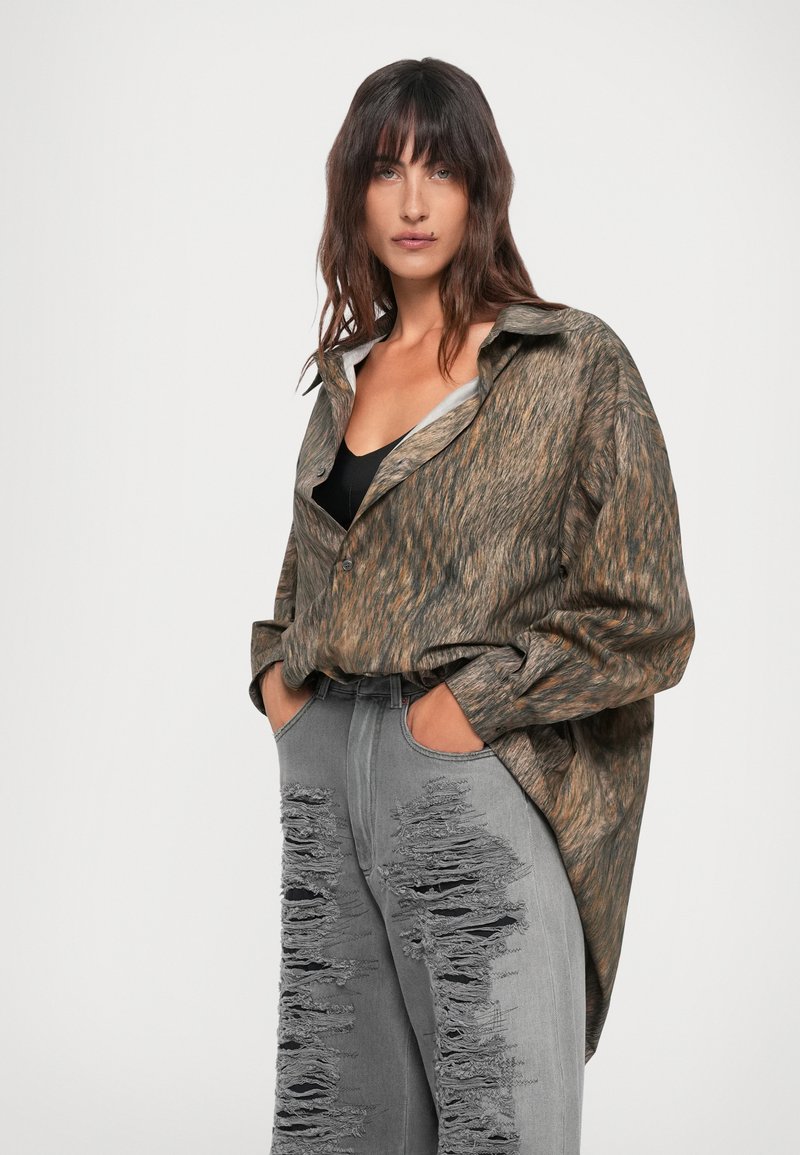 Överdimensionerad brun mönstrad skjorta med spetsig krage, kombinerad med högmidjade grå jeans med stora slitna lappar.