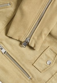 Béžová sukně z semiše s hladkou texturou, se stříbrnými zipovými uzávěry a detaily kapsy s drukovým knoflíkem na přední straně.