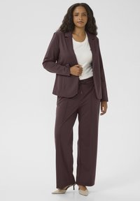 Veste cintrée bordeaux sur un top blanc et un pantalon large bordeaux assorti. Le tissu semble doux, avec des accents subtils et des lignes épurées.