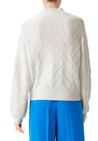 Weißer gestrickter Pullover mit strukturiertem Fischgrätmuster, gerippten Bündchen und Saum, von hinten gezeigt, kombiniert mit blauen Hosen.