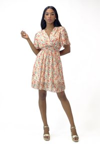 Robe florale en pêche clair avec des manches bouffantes courtes, une taille smockée et une jupe longueur genoux. Présente de petites fleurs multicolores et un tissu doux.